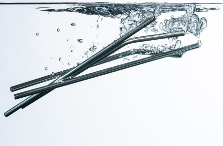 Silver straws submerged in clear water with bubbles rising around them.