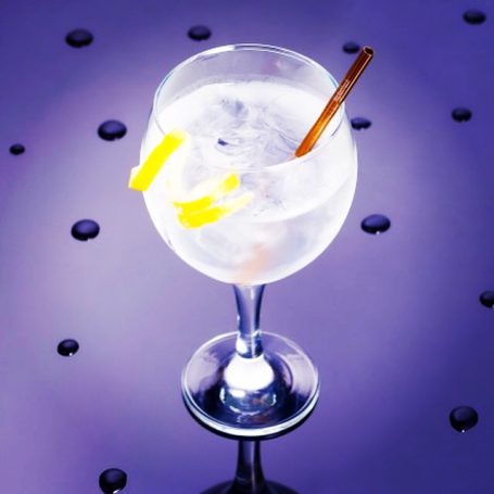 A refreshing cocktail in a glass, garnished with lemon and a bronze coloured straw.